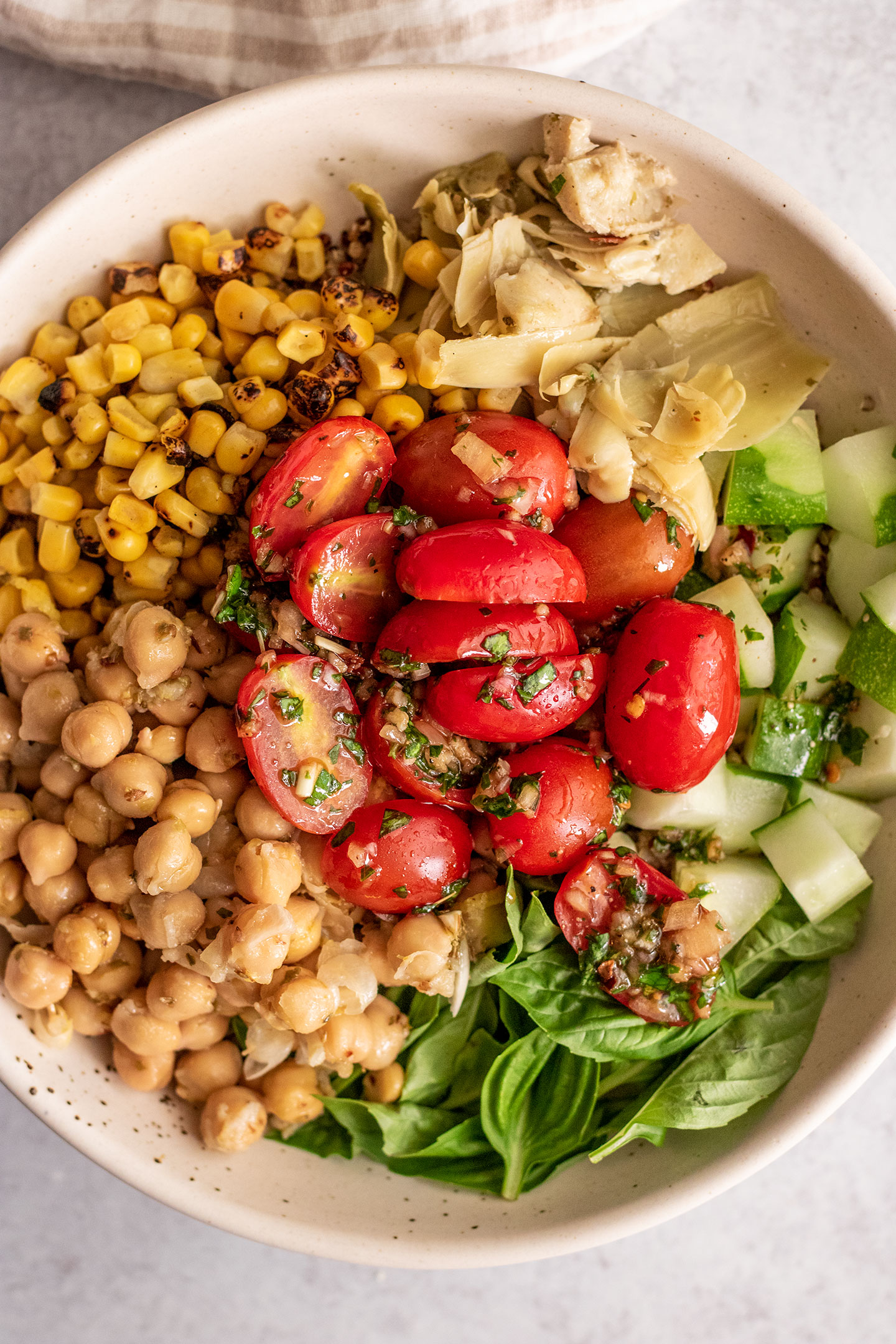 Giant bowl of quinoa topped with corn, chickpeas, artichoke hearts, cucumbers, basil and marinated cherry tomatoes.