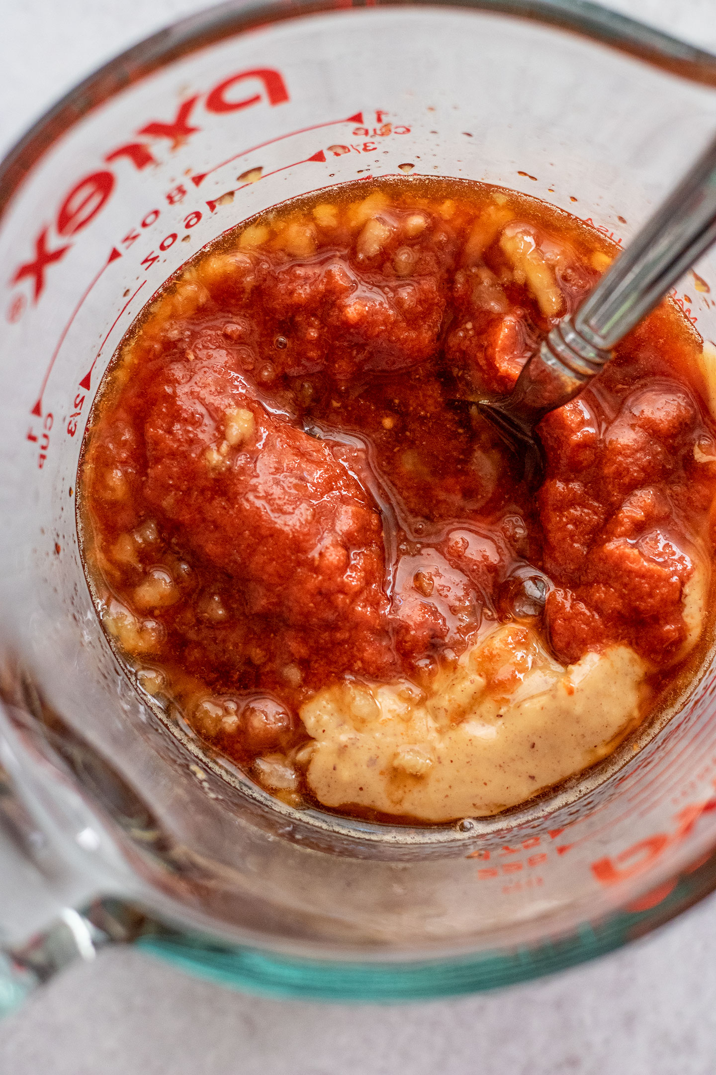 Mixing peanut butter and red curry paste together in a glass measuring cup.