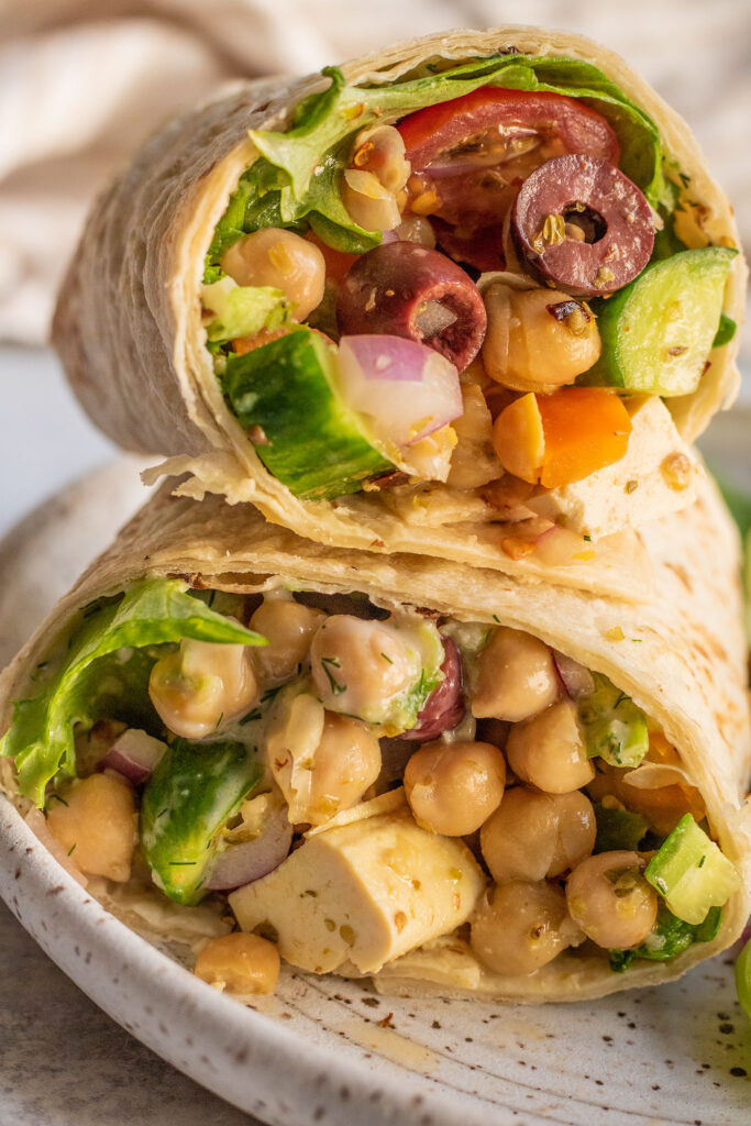 Close up of a stuffed chickpea and tofu wrap stacked on top of each other on a plate.