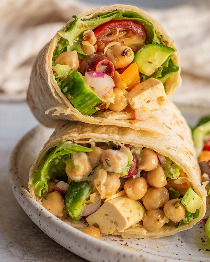 Cross section of a chickpea and tofu wrap loaded with vegetables and dressing, stacked on top of each other.