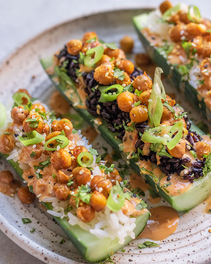 Side view of a plate of cucumber boats topped with chickpeas, scallions, cilantro and tahini sauce.
