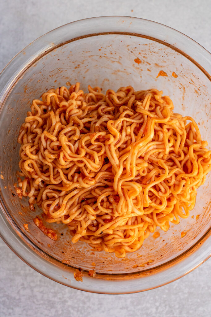 Tossing cooked noodles with gochujang sauce in a bowl.