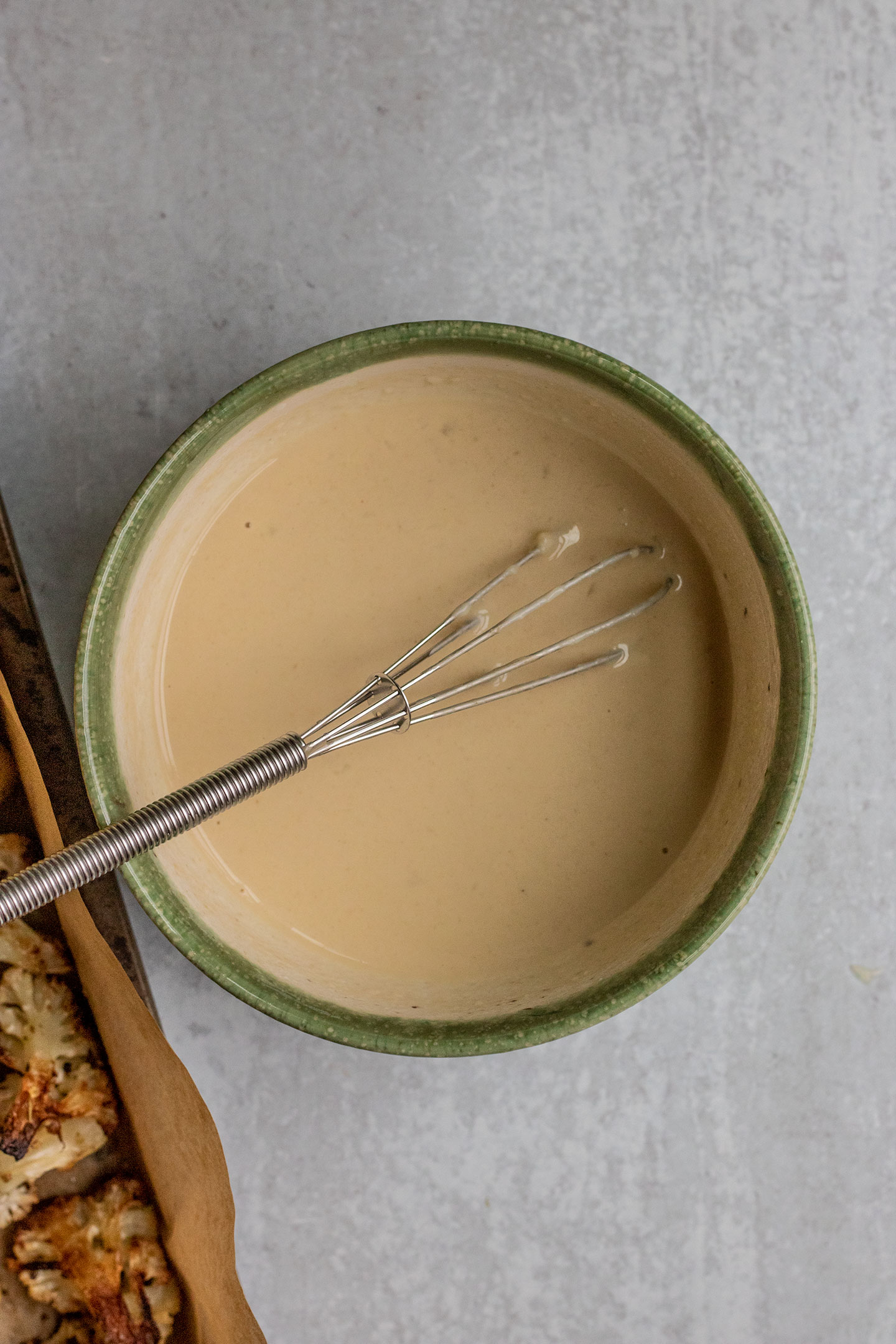Mixing the garlic and miso tahini dressing with a small whisk in a bowl.