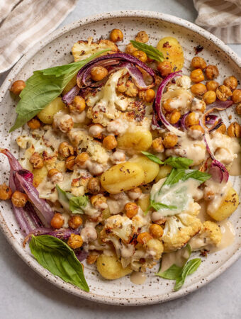 Plate of roasted cauliflower, gnocchi and onions topped with crispy chickpeas and garlic tahini sauce.