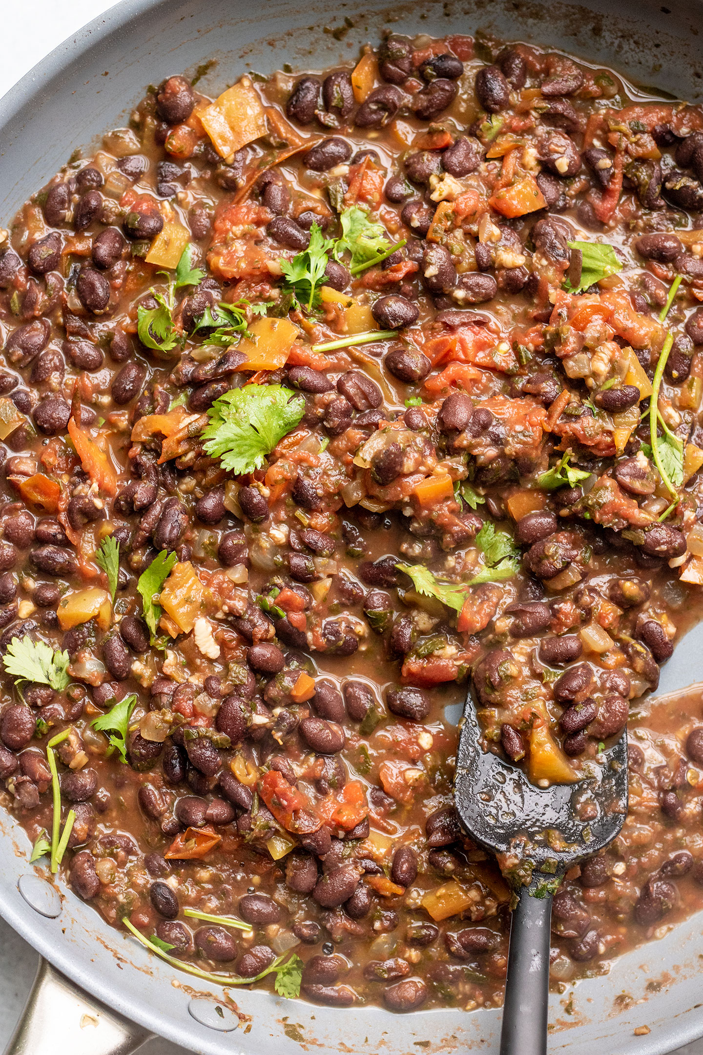 Thickened black beans in sofrito topped with fresh herbs in a large skillet.