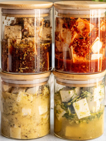 Four jars stacked on top of each other filled with 4 different marinades including balsamic tofu, gochujang tofu, tofu feta and cilantro lime tofu.