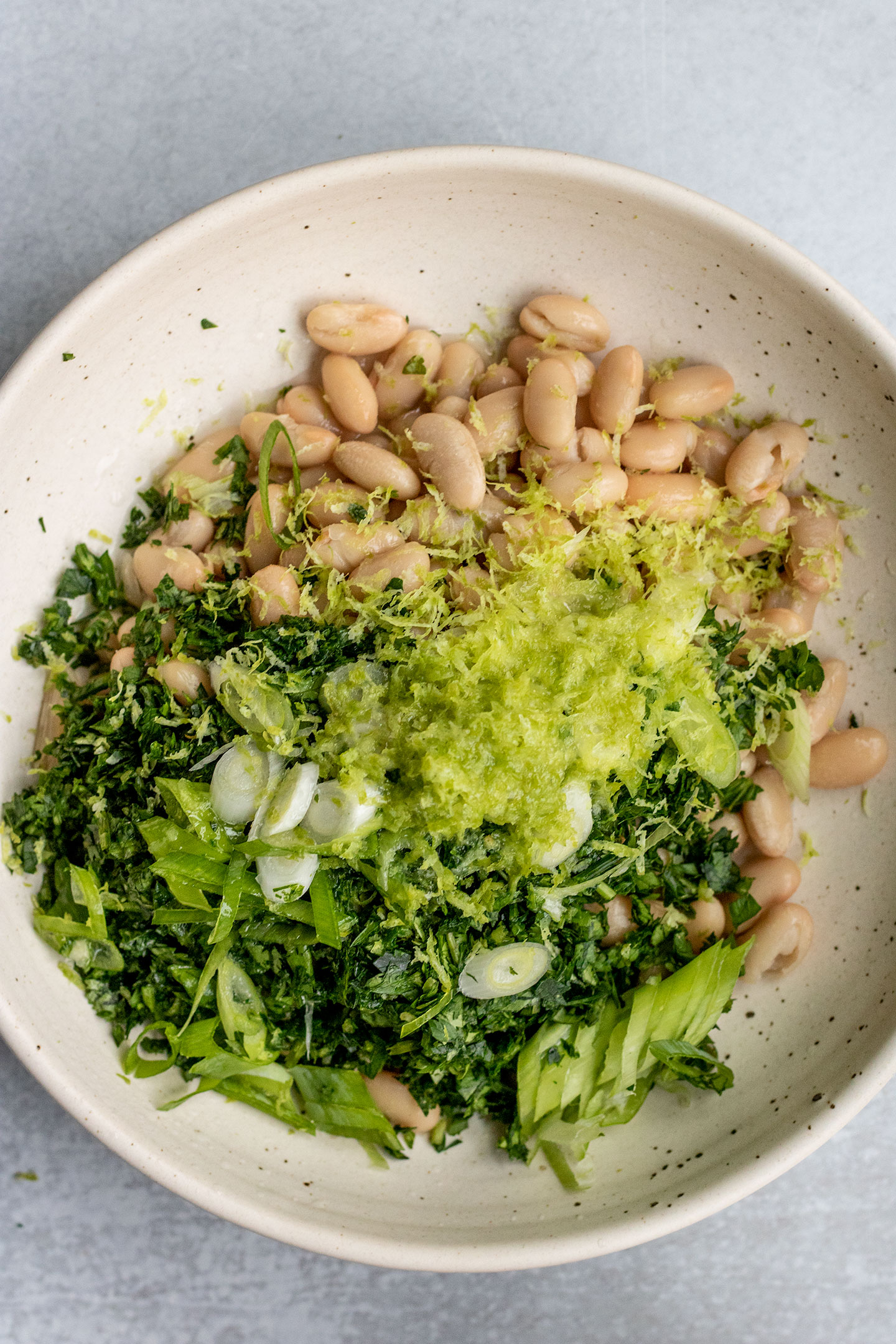 Bowl with white beans, scallions, herbs, lime juice and lime zest.