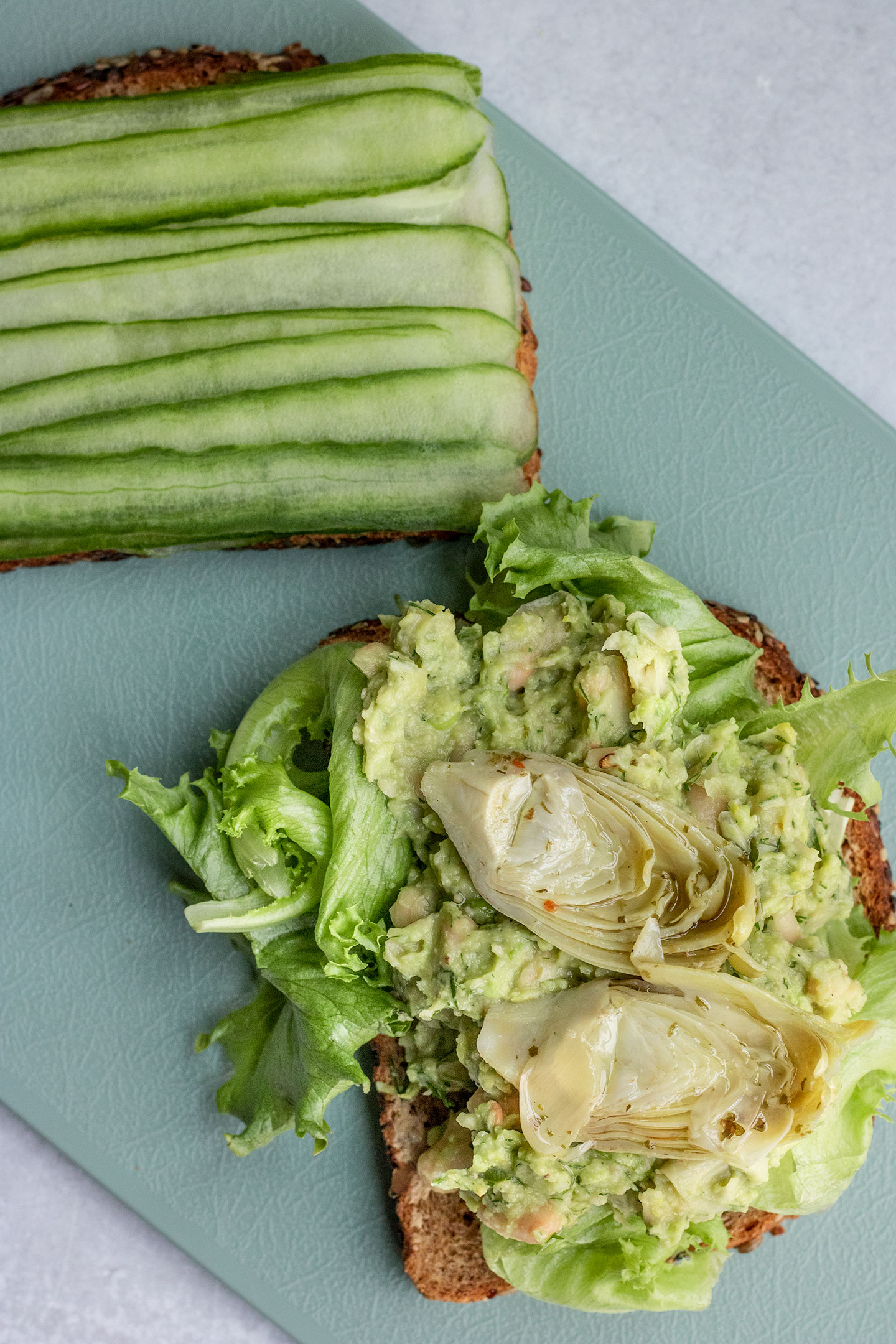 Assembling the avocado white bean spread on bread, greens, artichoke hearts and cucumber.