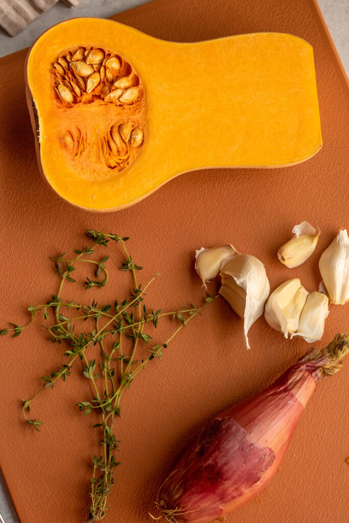 Butternut squash, garlic, shallot and thyme on a cutting board.