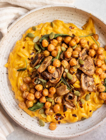 Creamy butternut squash orzo on a plate with sage infused mushrooms and crispy chickpeas on top.