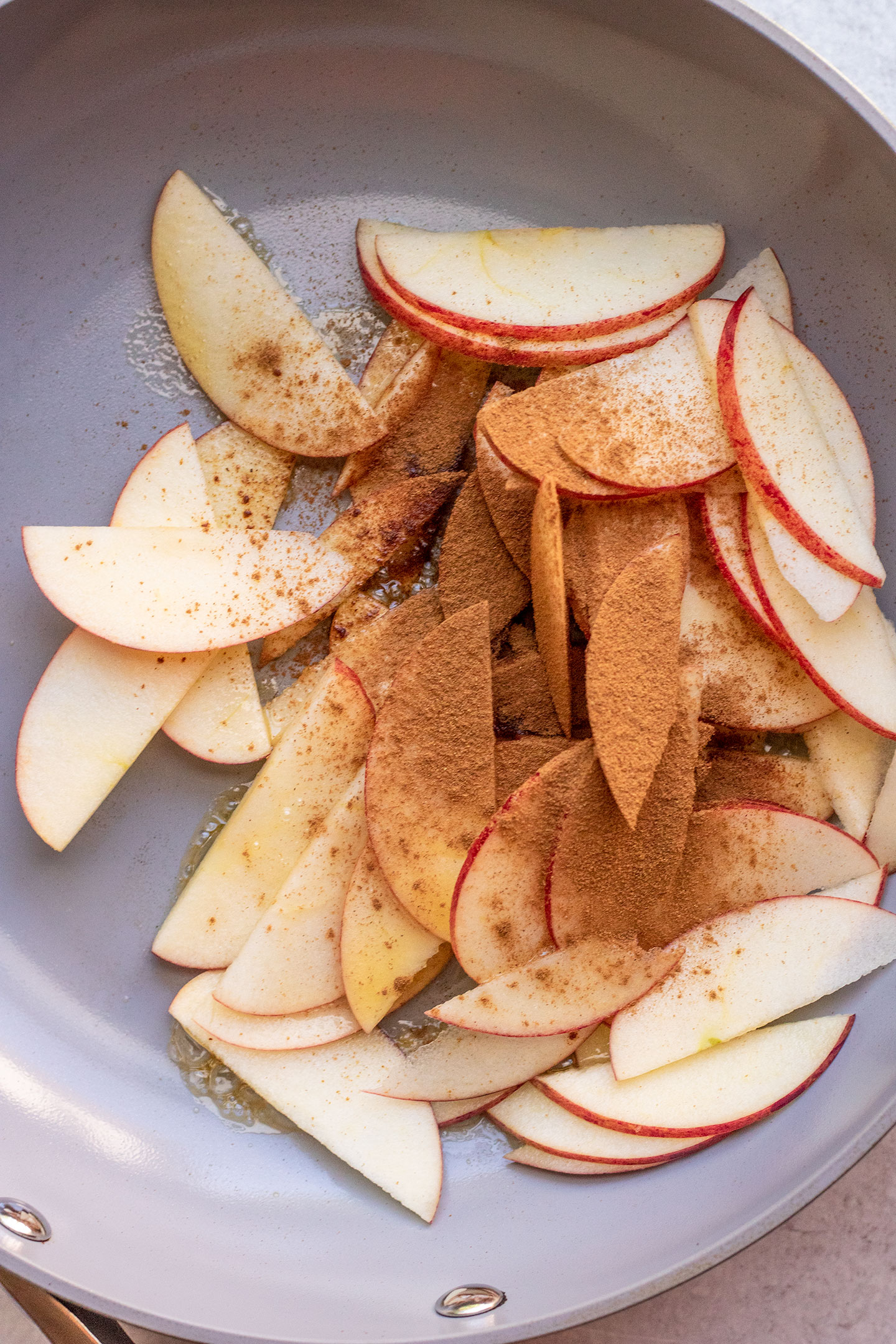 Apple slices added to a pan with cinnamon and maple syrup.