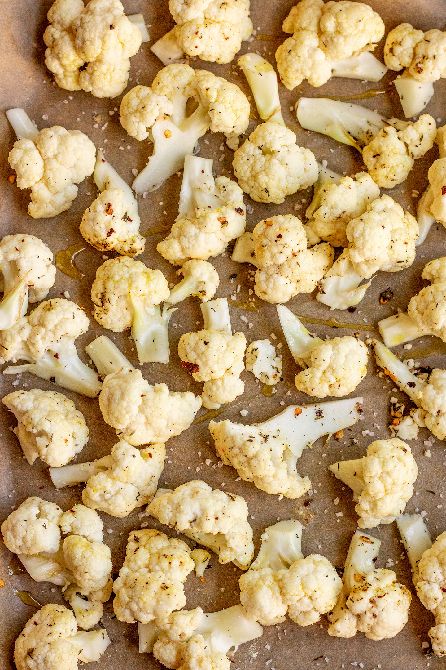 Cauliflower coated with oil and seasonings on a parchment lined baking tray.