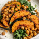 Close up side view of a plate of roasted acorn squash topped with crispy chickpeas and served over a smear of cashew cream and roasted kale.