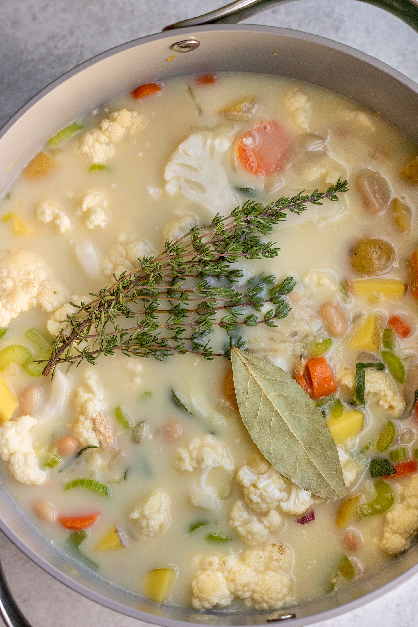 All of the pot pie soup ingredients added to a large soup pot and topped with thyme and bay leaves before simmering.