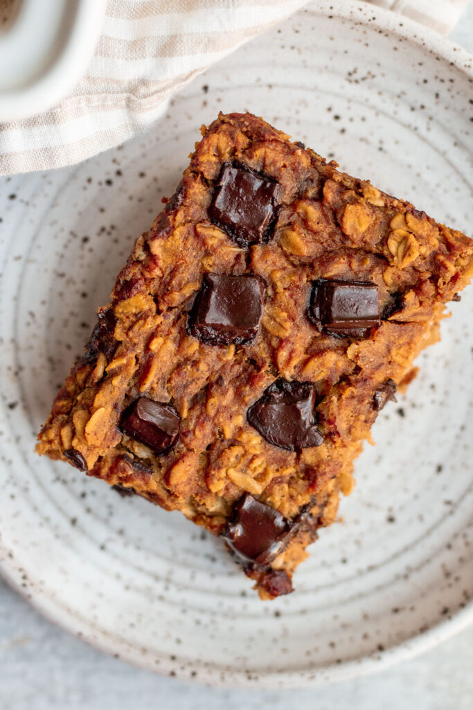 Top down view of a slice of pumpkin baked oatmeal loaded with chocolate chips on a white plate.