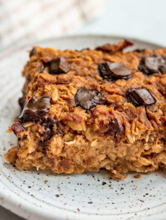 Close up shot of a slice of pumpkin baked oats on a plate loaded with chocolate chips.