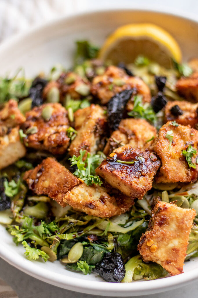 Side view of crispy oven roasted tofu on top of a bed of roasted brussels sprouts and kale.