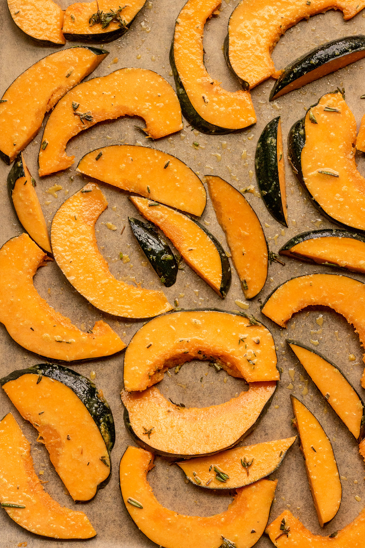 Garlic rosemary coated acorn squash spread out on a parchment lined baking tray.
