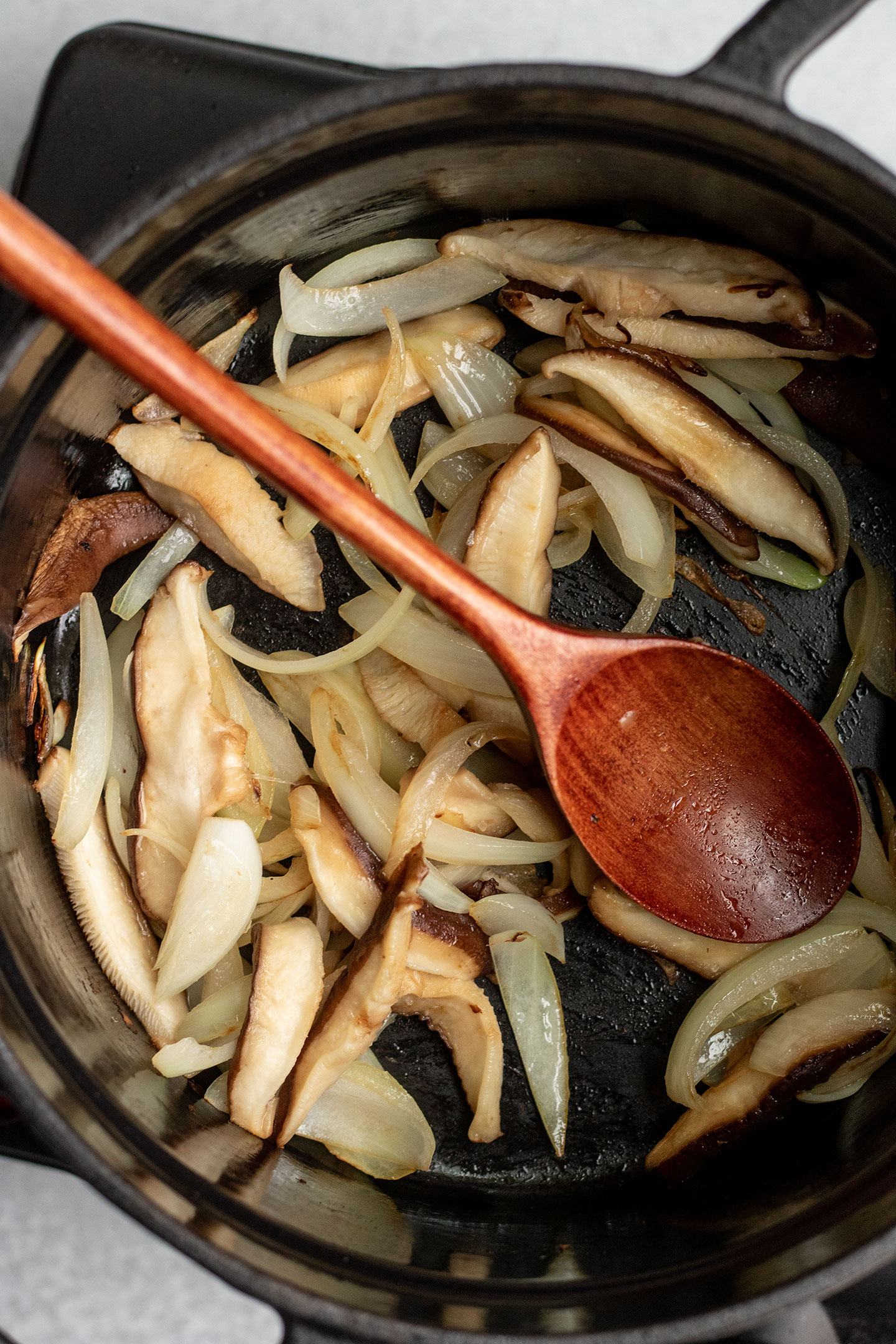 Stirring the onions and shiitake mushrooms together in a pot with a wooden spoon.