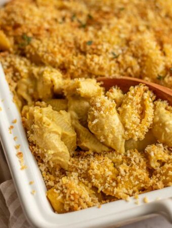 Spooning out a portion of small shells coated in butternut squash cashew cheese sauce with breadcrumb topping.