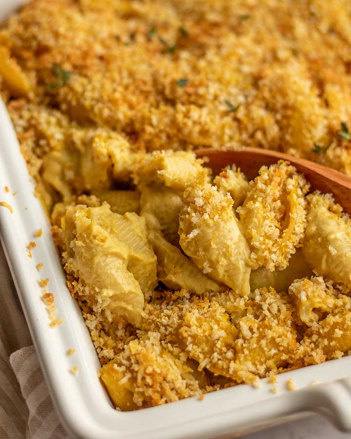 Spooning out a portion of small shells coated in butternut squash cashew cheese sauce with breadcrumb topping.