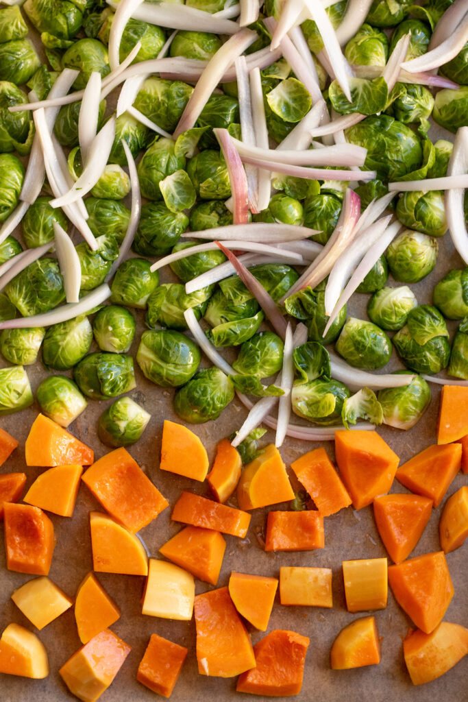 Sheet pan with brussels sprouts halves and shallots on one side and butternut squash on the other side.