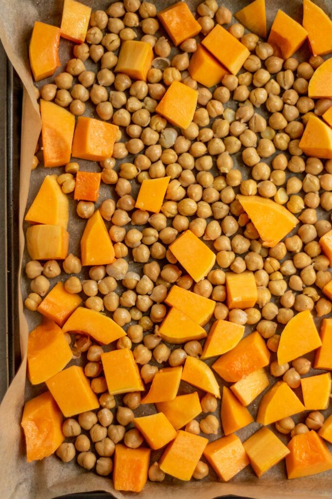 Chickpeas and butternut squash coated in oil and spread out on a baking tray.