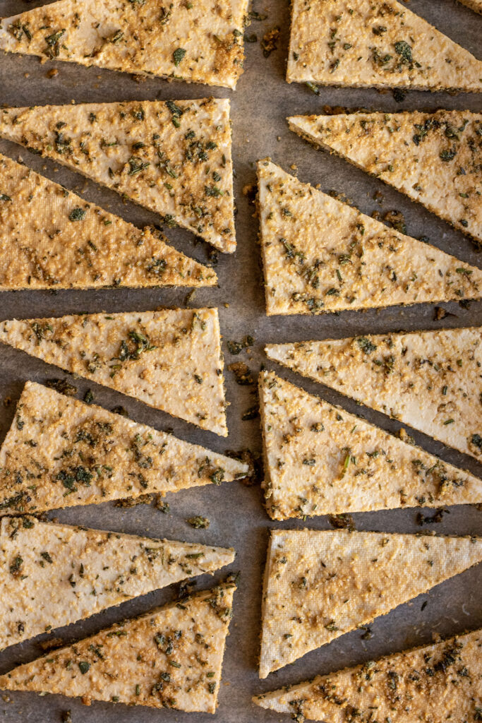 Cornmeal, herbs and seasonings coated on tofu triangles sitting on a baking tray.