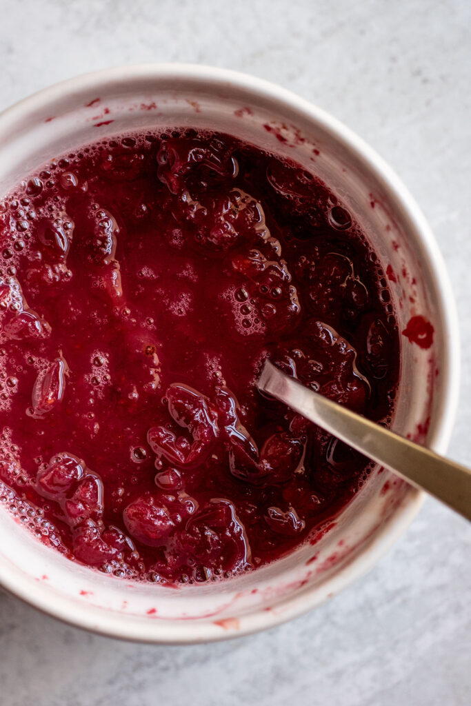 Mashing together the baked cranberries and orange juice in a ramekin.