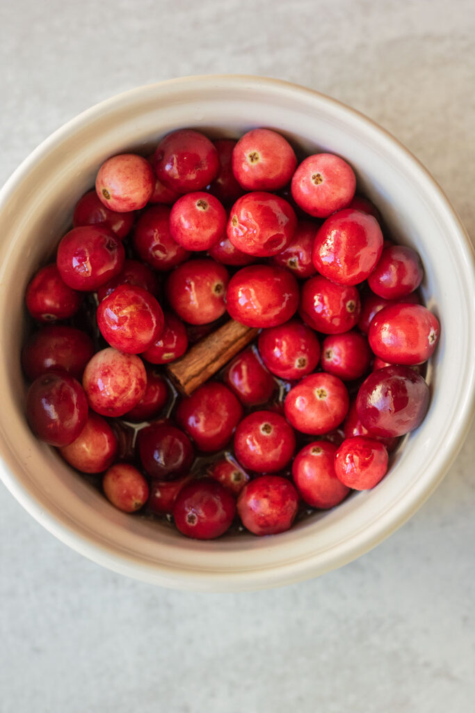 Combining the cranberries, maple syrup, water and cinnamon stick together in a ramekin.