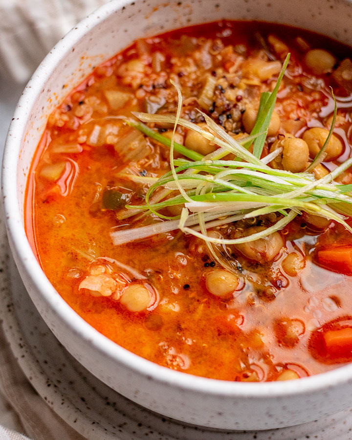 Close up view of a side angle of a white bowl of gochujang soup topped with shredded scallions.