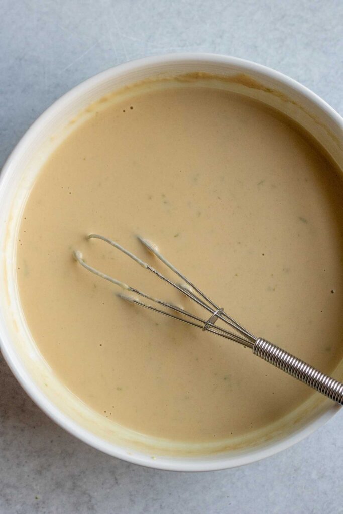 Whisking the maple lime tahini sauce together in a small white bowl.