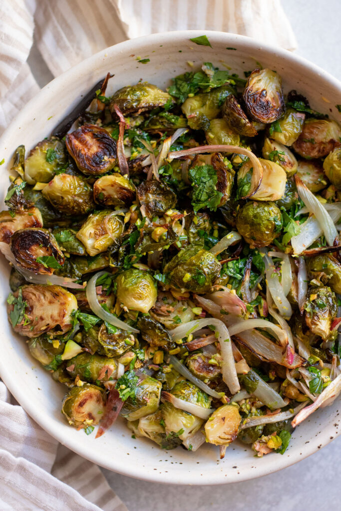 Roasted brussels sprouts tossed with chopped pistachios, shallots, lime and parsley in a bowl.