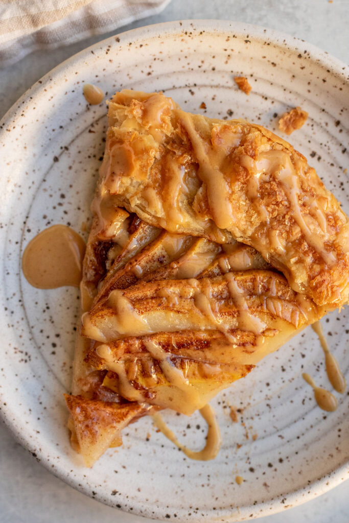A slice of puff pastry pear galette on a plate drizzled with extra sweet peanut miso sauce.