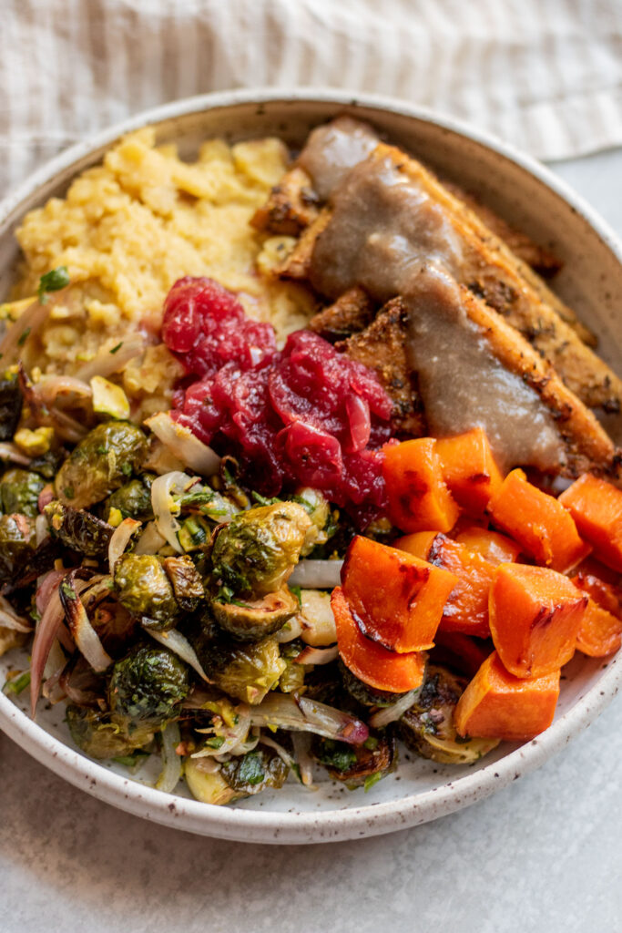 Side view of a bowl of mashed potatoes, cranberry sauce, baked tofu, brussels sprouts and baked squash. 