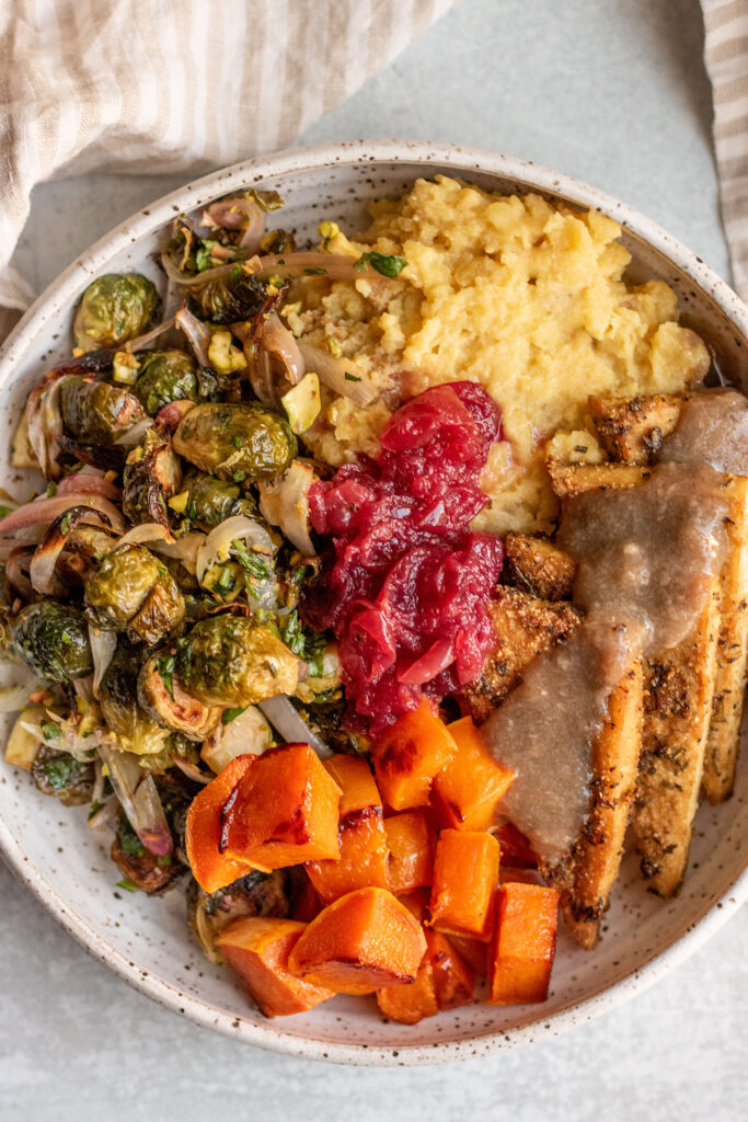 Bowl of mashed potatoes, roasted brussels sprouts, butternut squash, baked tofu and cranberry sauce. 