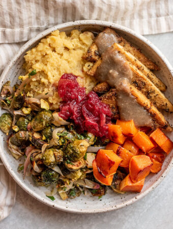 Close up of a bowl of Thanksgiving food including cornmeal crusted tofu, mashed potatoes, brussels sprouts, butternut squash and cranberry sauce.