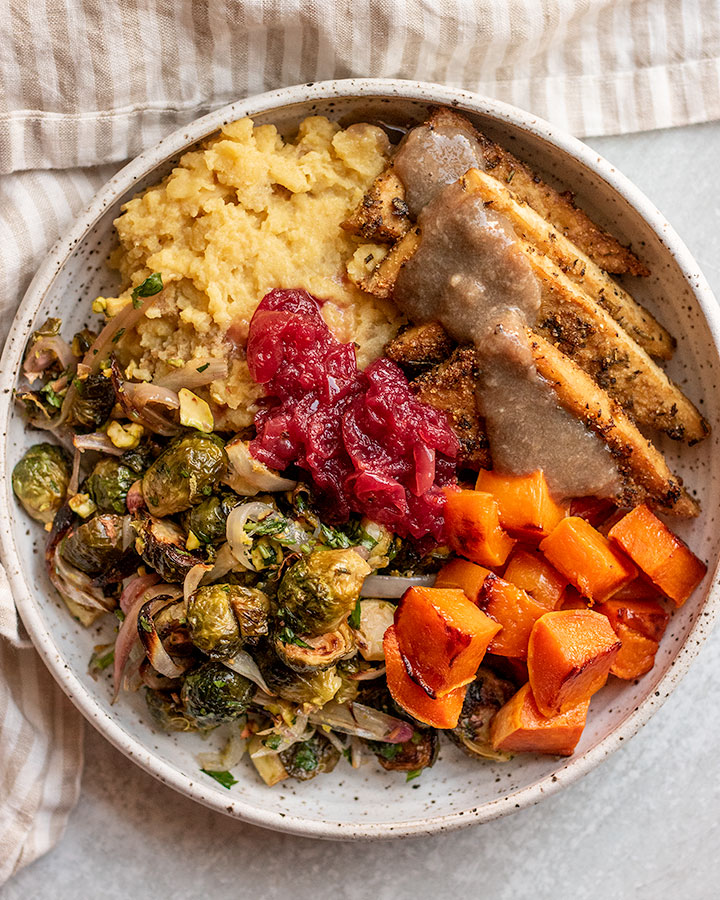 Bowl filled with sheet pan mashed potatoes, tofu, brussels sprouts, butternut squash and cranberry sauce.