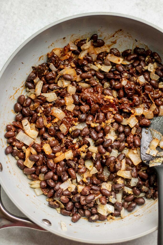 Mixing the chipotle peppers, seasonings with the black beans and onions in a pan.