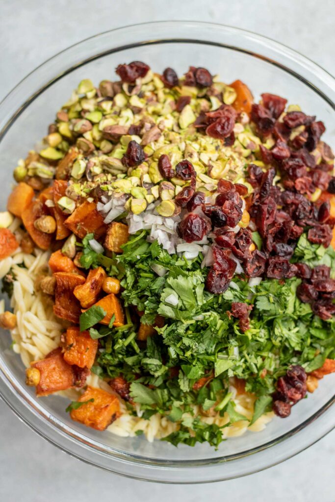Bowl filled with roasted kale, orzo, roasted butternut squash and chickpeas, parsley, cranberries, and pistachios.