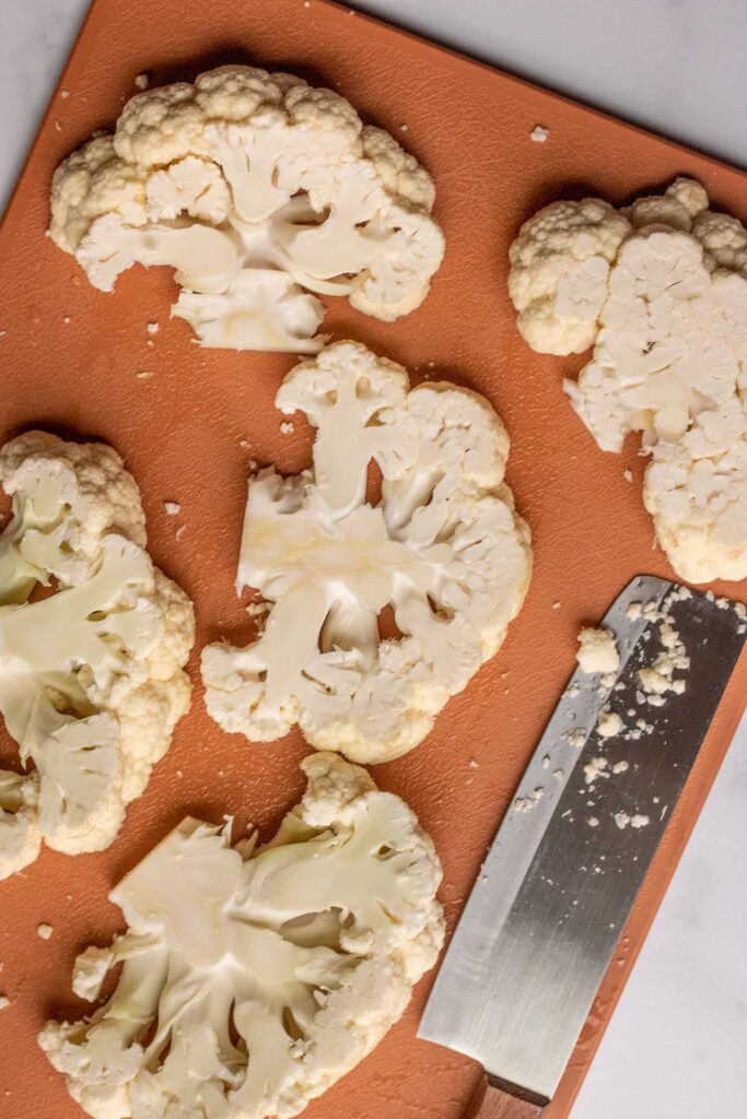 Cutting cauliflower heads into thin slabs on a cutting board.