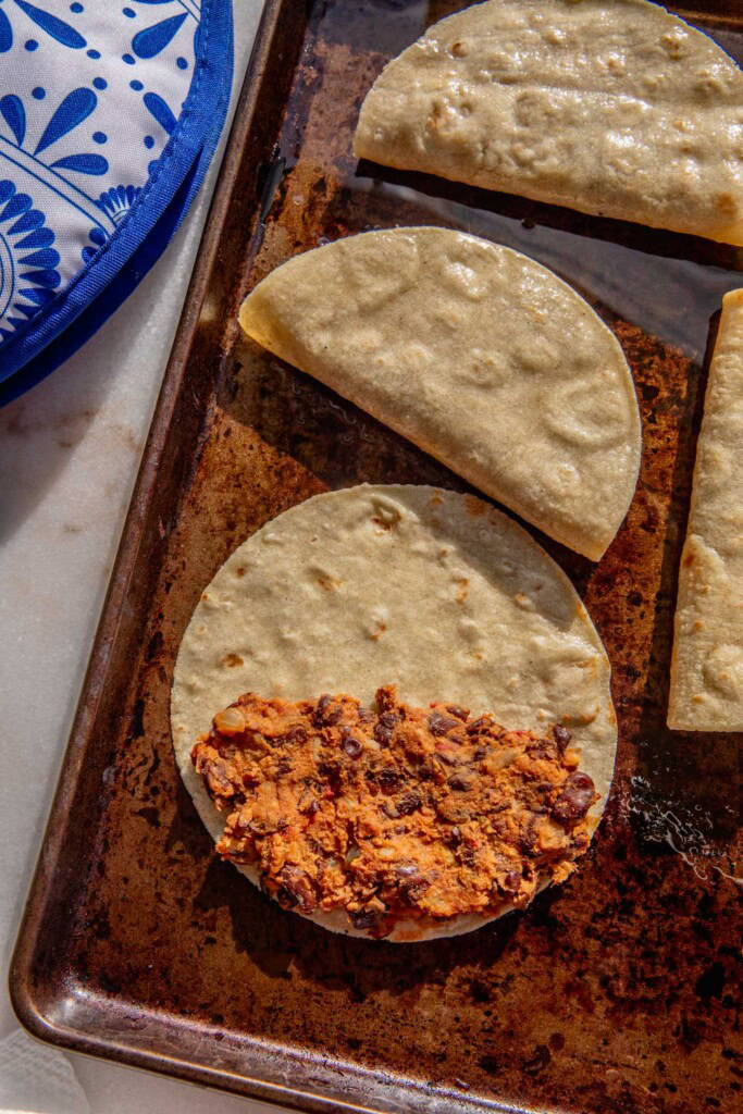 Baking tray with tortillas stuffed with black bean filling.