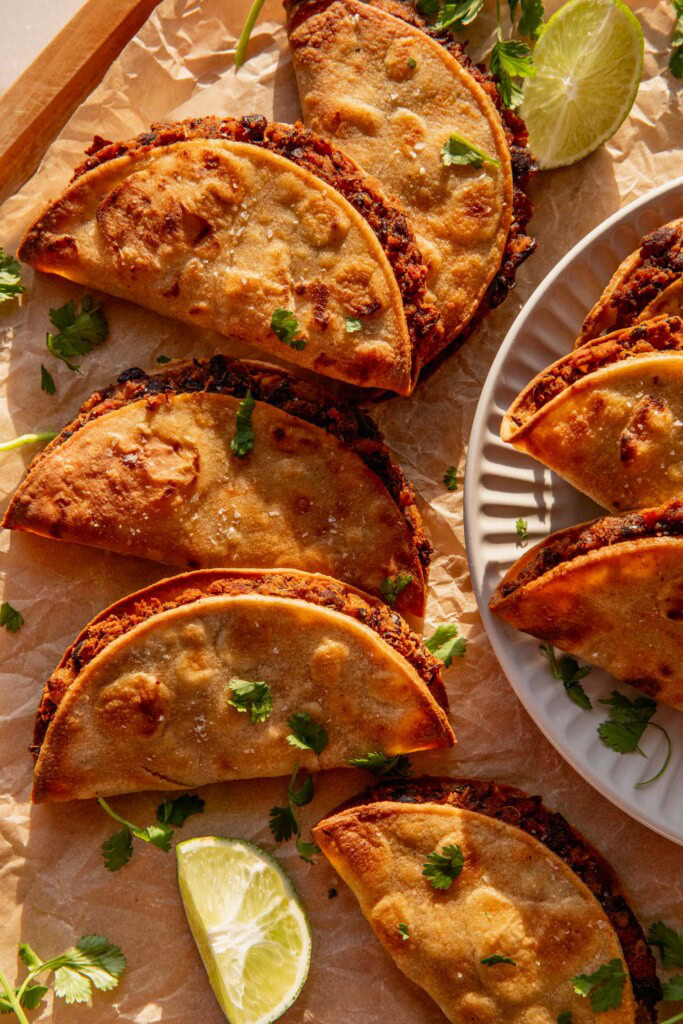 Close up of a pile of tacos sitting next to a plate of tacos on the side.
