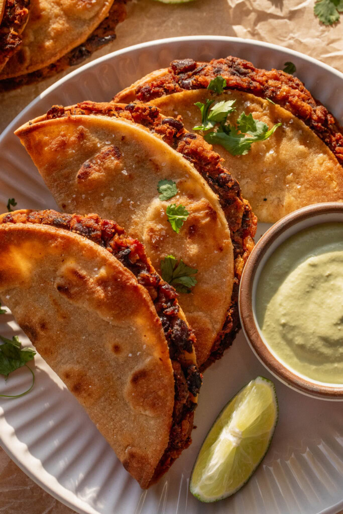 Close up of a plate filled with 3 crispy black bean tacos and jalapeno crema.