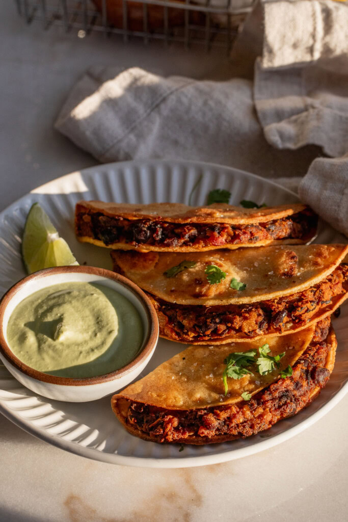 Plate with 3 stacked black bean tacos and a dish of jalapeno cream for dipping.