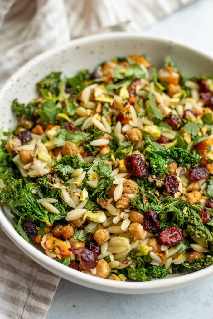 Side view of a close up bowl of kale orzo salad mixed with maple lime vinaigrette.