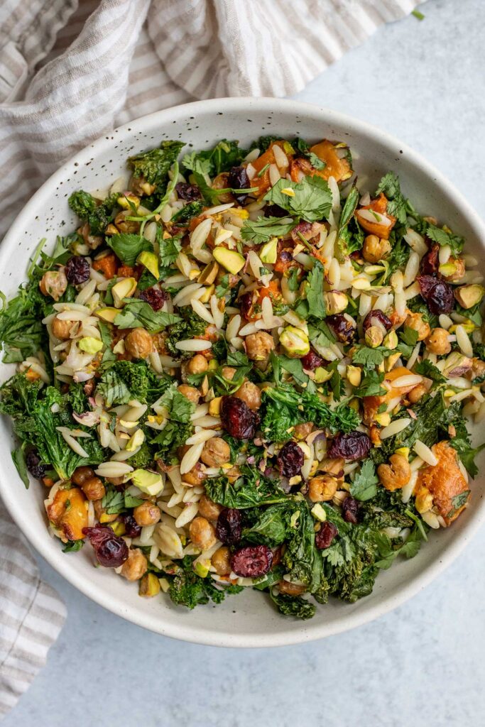 Top down view of a bowl of orzo salad mixed with chickpeas, kale, pistachios and dried cranberries.