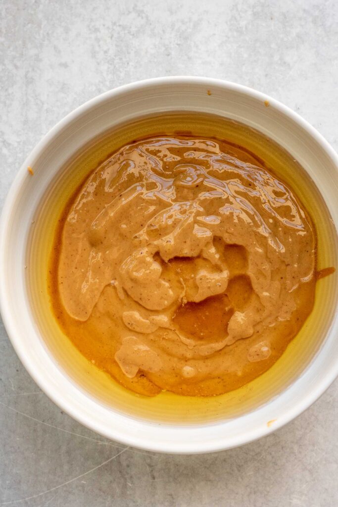 Mixing peanut butter and maple syrup in a small white bowl.