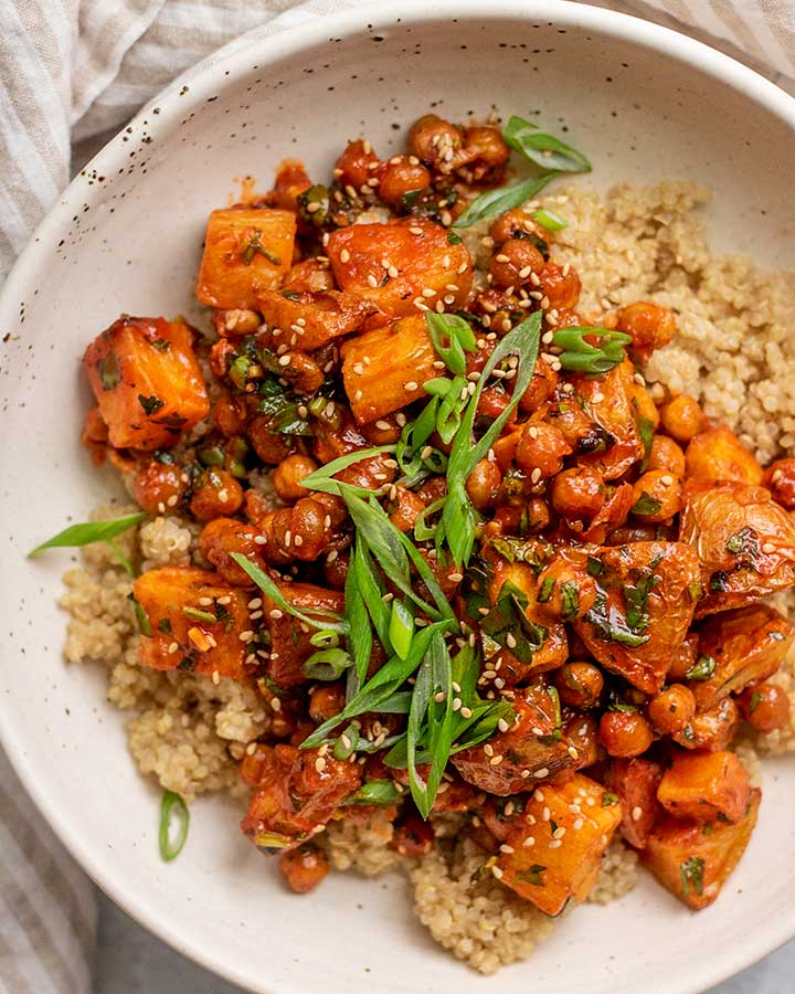 Close up of a bowl of gochujang potatoes and chickpeas topped over rice and served with extra scallion slices on top.