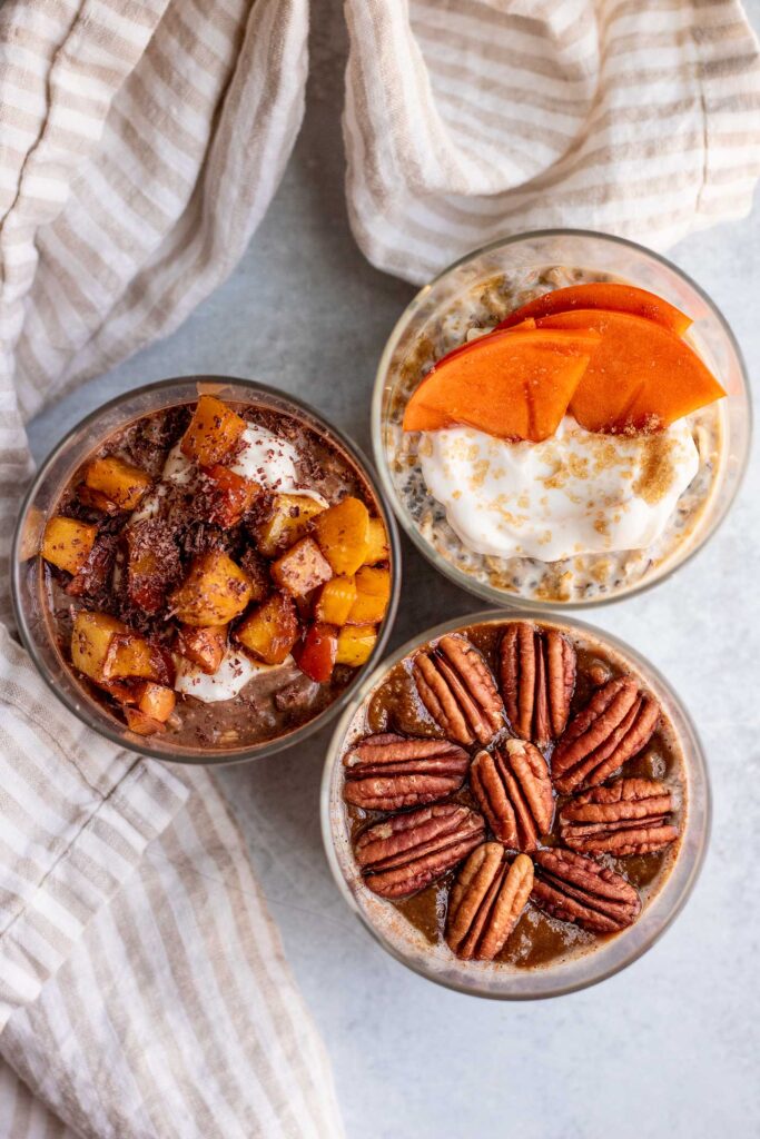 Top down view of one jar topped with yogurt and persimmons, a second jar topped with pecans, and the last jar topped with yogurt and sauteed pears.